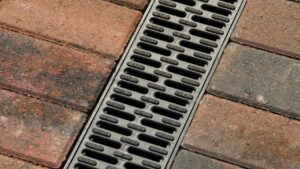 Close-up of a metal trench drain grate set in red and gray brick pavement