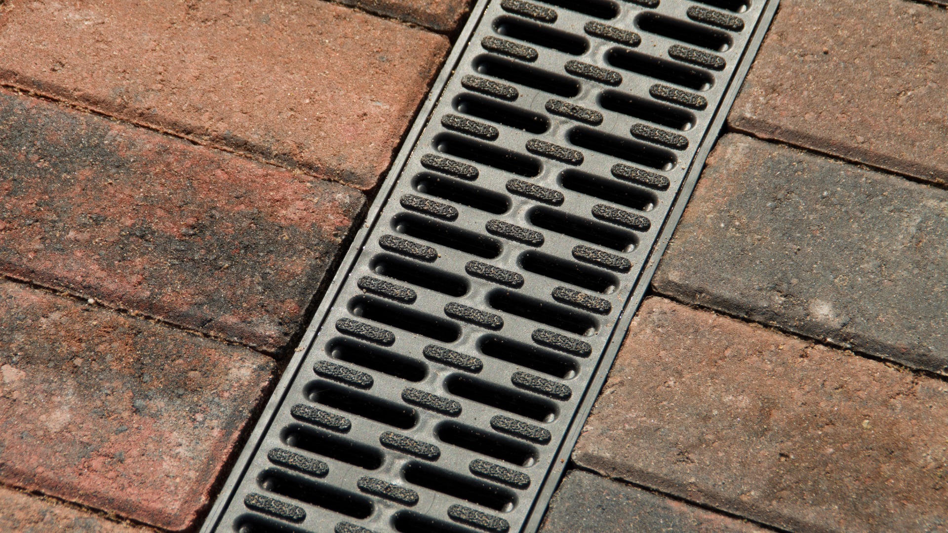 Close-up of a metal trench drain grate set in red and gray brick pavement